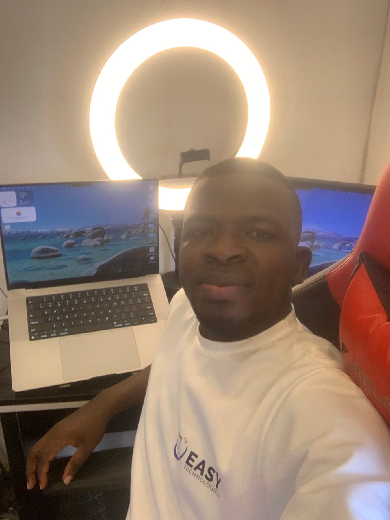 Israel Afolabi at his desk with laptop and monitor, wearing an EasyTech shirt